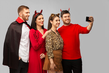 Sticker - friendship, holiday and people concept - group of happy smiling friends in halloween costumes of vampire, devil and cheetah taking selfie by smartphone over grey background