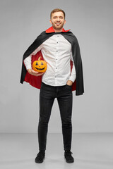 Poster - holiday and people concept - happy smiling man in halloween costume of vampire and dracula cape holding jack-o-lantern pumpkin over grey background