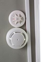 Two white smoke detector and fire sprinkler on a light ceiling. Vertical orientation. Fire alarm.