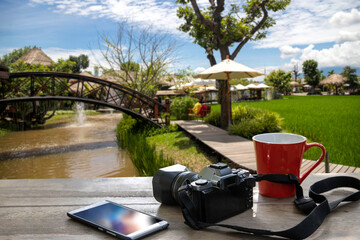 red cup of coffee with retro camera and mobile phone on wooden table in nature background