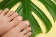 Female feet with pink nail design. Pink nail polish pedicure on yellow background.