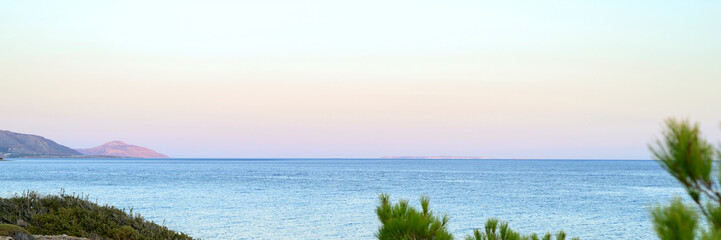 seascape at dusk. a dirt road, a city in the distance and mountains with a gentle pink sunset and a beautiful blue sea. banner