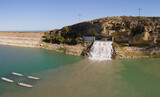 Fototapeta Na ścianę - A waterfall on a reservoir above Crevillente. The water flows into the lake. In the background on the horizon the Mediterranean Sea with blue skies in summer.