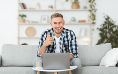 Happy handsome man sitting on couch showing thumb up