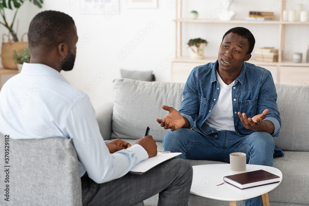 Stressed black man explaining his problems to psychologist at individual therapy session - obrazy, fototapety, plakaty 