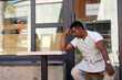 upset african man sit in the street, his cafe shop is crashing, it is closed, in crisis. black man doesn't know how to solve problem with clients and sale, no customers.