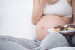 © nareekarn - beautiful young pregnant woman holding sweet donut in her hand. expectation of the child, pregnancy and motherhood. healthy and unhealthy eating concept, diet. Junk food. soft focus background
