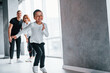 © standret - Woman in formal clothes and with camera in hand standing inside of empty room with man and little boy that running and having fun