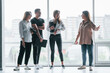 © standret - Woman holding her professional camera. Group of business people in formal clothes standing indoors near big window