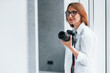 © standret - Woman in formal clothes and with camera in hand standing inside of empty room