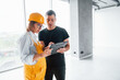 © standret - Female worker or engineer in yellow uniform and hard hat standing indoors with man