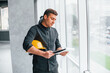 © standret - Male worker or engineer with yellow hard hat standing indoors with notepad
