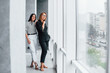 © standret - Two business women standing together indoors in the office near big window