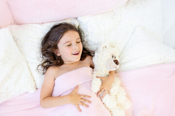 morning of a little girl 5-6 years old, a girl yawns in bed with a teddy bear