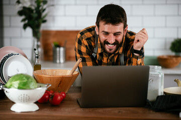 Wall Mural - Portrait of handsome man in kitchen. Young man cooking while having video call.