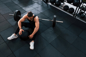 Strong man in sportive clothes sitting on the floor in the gym with equipment