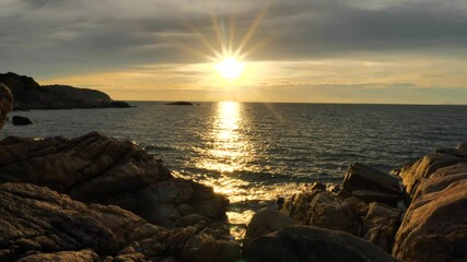 Wall Mural - Amazing Sun Rays at Sunset time above the ocean, water surface at rocky coast in slow motion at sunset time, nature background static shot