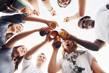 View from below. Doing cheers. Group of young people in casual clothes have a party at rooftop together at daytime