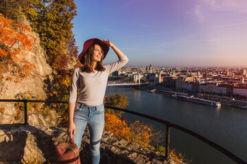 Wall Mural - A happy young woman enjoying her trip to Budapest, Hungary from the point from Gellert Hill during sunrise in autumn during sunrise.