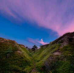 Scenic ravine with green grass and trees under beautiful sunset sky with clouds.