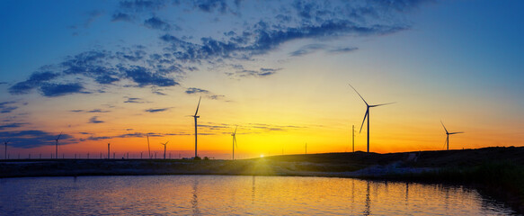 Wall Mural - silhouettes of wind generators power plant on lake at sunset
