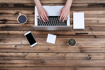 Wall Mural - Female hands typing on laptop keyboard with notepad, smartphone and cup of coffee