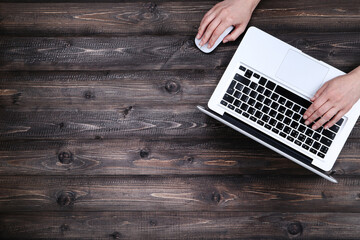 Poster - Female hands typing on laptop keyboard and using mouse on wooden table