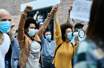 Wall Mural - Two black women with face masks holding hands while participating in public demonstrations.