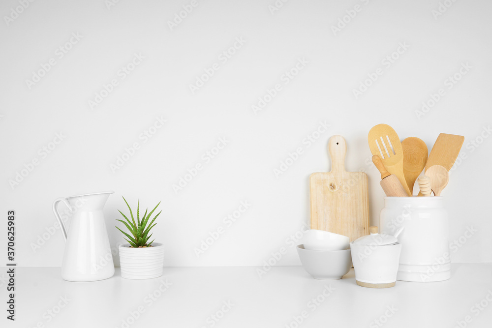 Kitchenware and utensils on a white shelf or countertop with a white wall background and copy space. Home kitchen cooking decor. - obrazy, fototapety, plakaty 