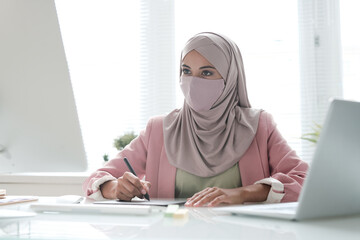 Poster - Young Muslim businesswoman in hijab sitting at desk and using computer and digitizer while working on digital design in office