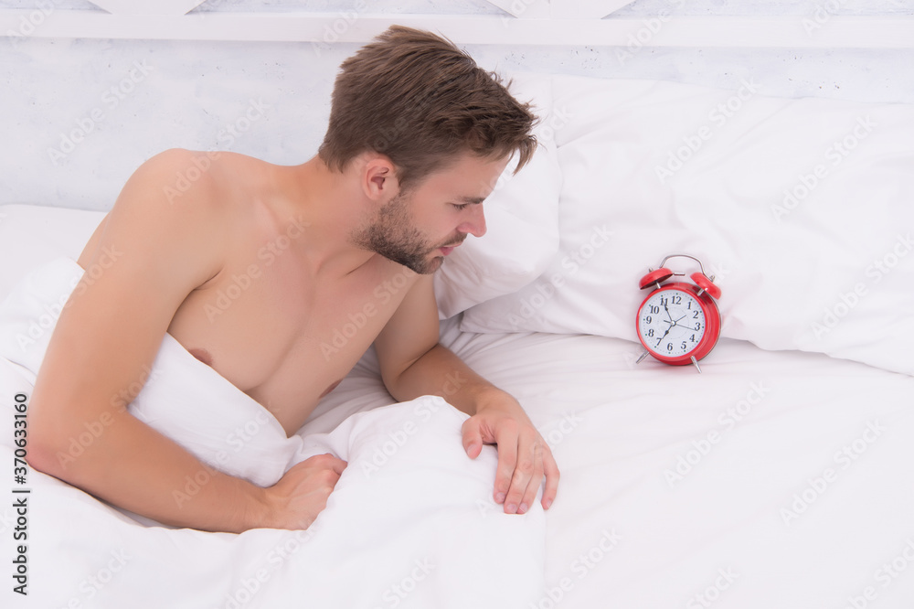 Sleepyhead. Sexy man check time in bed. Unshaven man lying in bed ...