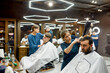 © Svitlana - Working in barbershop. Professional young barber girl drying hair of young handsome bearded man visiting modern barbershop