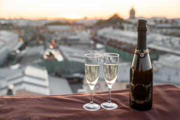 A bottle and two glasses of champagne and against the backdrop of city rooftops at sunset