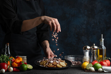 Wall Mural - The chef prepares a dish of potatoes with octopus sprinkling with sliced ​​octopus pieces, freezing in motion, cooking seafood dishes, gastronomy and culinary, recipe book