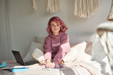 Happy Hipster Teen Girl School Gen Z College Student With Pink Hair Wears Hoodie Sits On Bed With Laptop Books Learning Exam Looking At Camera At Home. Generation Z Teenager Portrait.