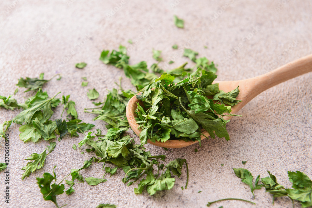 Spoon with dry parsley on grey background