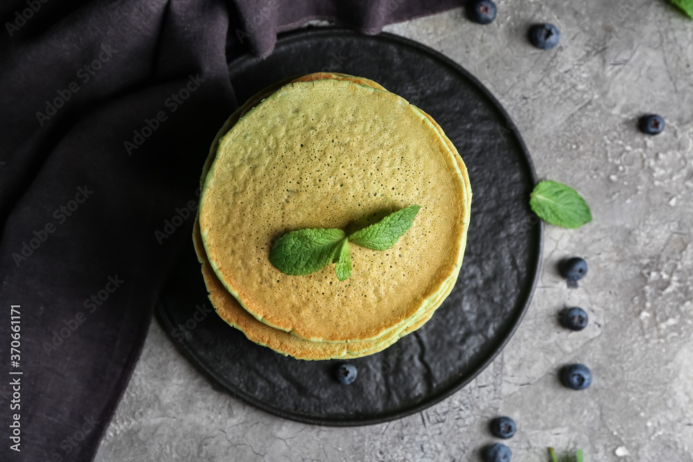 Plate with tasty green pancakes and berries on grey background