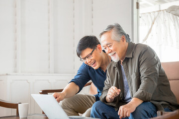 Happy senior asian father and adult son using computer laptop talking on video call in living room