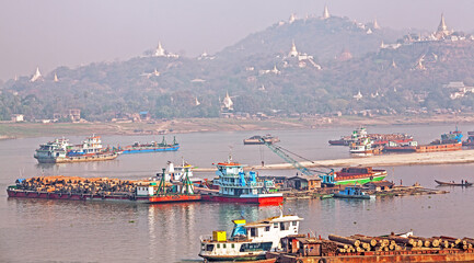 Loading teak wood onto barges and transportation along the Irrawaddy river at sunrise. Suburb of Mandalay, Myanmar