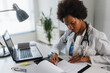 © lordn - Woman doctor with stethoscope looking at medical papers at her office working hard