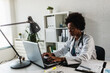 © lordn - Woman doctor with stethoscope looking at medical papers at her office working hard