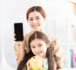 © Tom Wang - happy mother and daughter showing the mobile phone and piggy bank