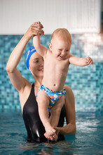 Vertical Snapshot Of A Smiling Mother Holding Her Baby Boy Over Water In Swimming Pool During Swim Exercises For Toddlers. Concept Of Early Development
