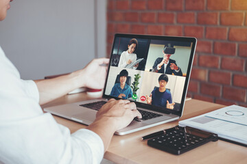 Wall Mural - Asian man working from home use Smart working and video conference online meeting with Asian team using laptop and tablet online in video call for new projects