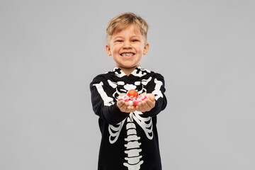 Wall Mural - halloween, holiday and childhood concept - smiling boy in black costume of skeleton with candies trick-or-treating over grey background