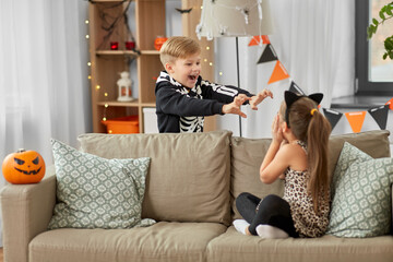 Wall Mural - halloween, holiday and childhood concept - smiling little boy and girl in costumes playing and having fun at home