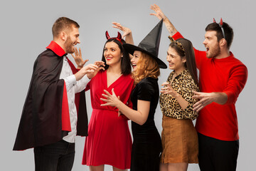 Wall Mural - friendship, holiday and people concept - group of happy smiling friends in halloween costumes of vampire, devil, witch and cheetah scaring each other over grey background