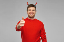 Holiday, Theme Party And People Concept - Happy Smiling Man In Halloween Costume Of Devil Showing Thumbs Up Over Grey Background
