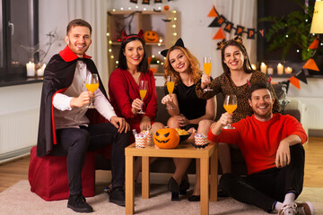 Wall Mural - friendship, holiday and people concept - group of happy smiling friends in halloween costumes of vampire, devil, cat and cheetah with non-alcoholic drinks at home party at night