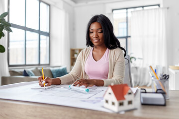 Poster - architecture, building, construction and real estate concept - happy smiling african american female architect with blueprint, ruler and living house model on table working at home office